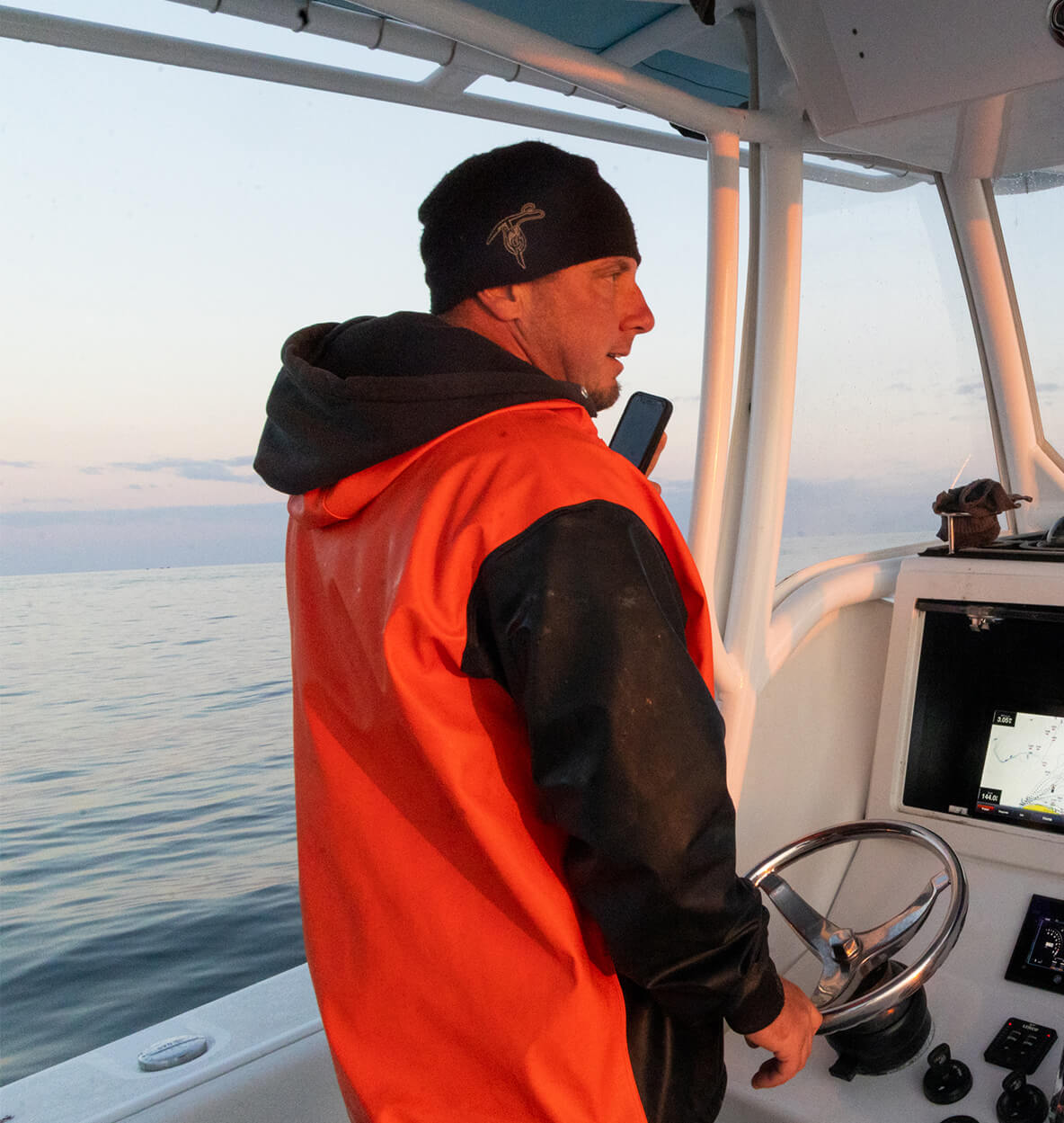 Matt Perchio is standing on a boat, with his back towards the camera. He is holding up his cellphone. 